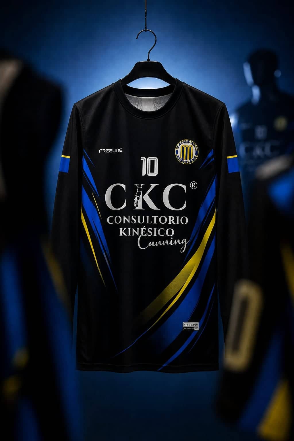 Camiseta negra con vivos azules y amarillos colgada de una percha, con el escudo de una institución en el pecho y el nombre del sponsor debajo.